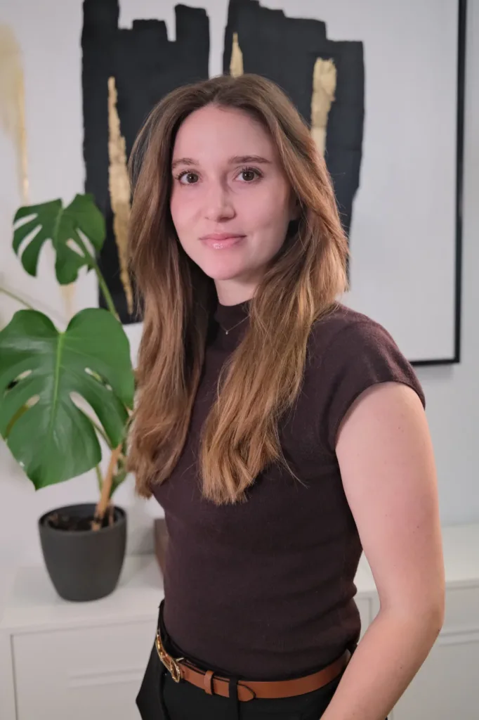 Lena Seidel steht lächelnd vor einem modernen Hintergrund mit einer Pflanze und abstrakter Kunst