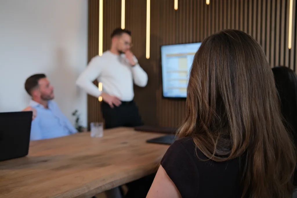 In einem modernen Besprechungsraum diskutiert das Team von BetonGold Immobilien konzentriert über Kapitalanlage-Immobilien, während eine Präsentation an die Wand projiziert wird