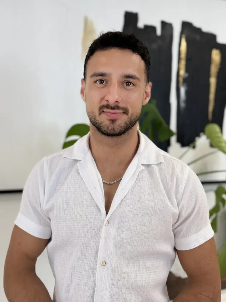 Can Cevir steht in einem modernen Büro von BetonGold Immobilien, lächelt freundlich und strahlt Professionalität aus