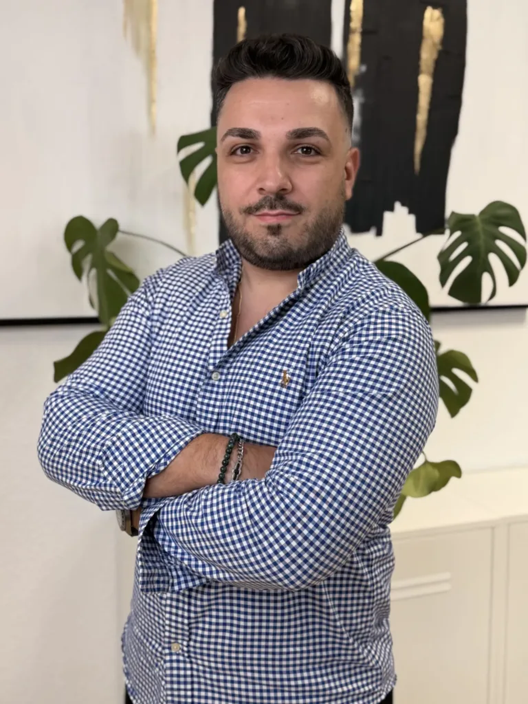 Marco Cirulli posiert mit verschränkten Armen vor einer modernen Wandgestaltung und Pflanze, im Hintergrund Geschäftsräume