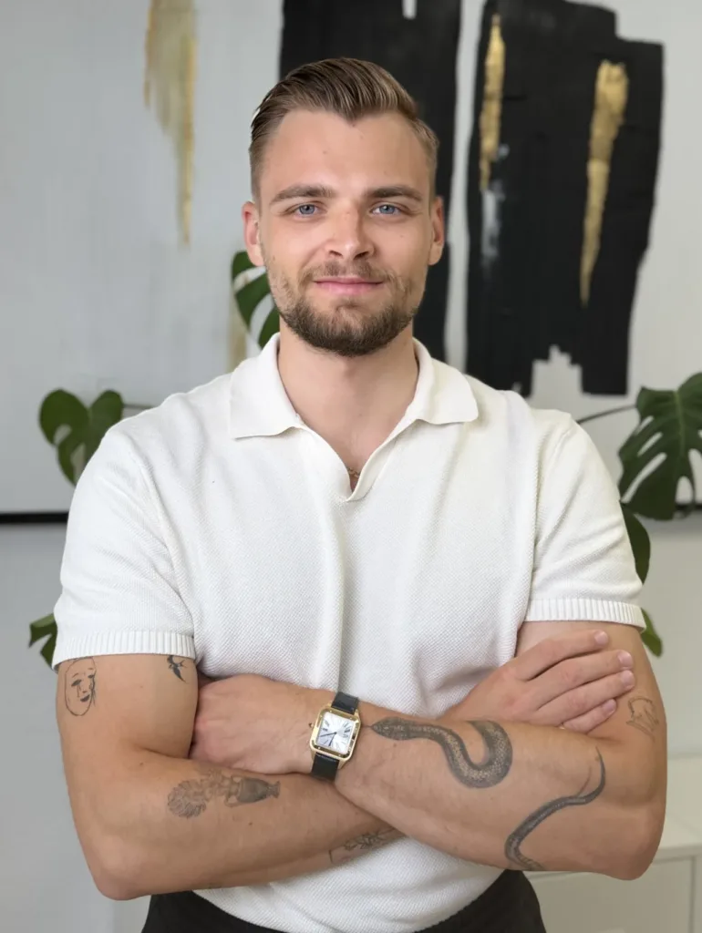 Mike Neues Bild steht mit verschränkten Armen in einem modernen Büro, das durch eine stilvolle Wandgestaltung und Pflanzen eine professionelle Atmosphäre ausstrahlt