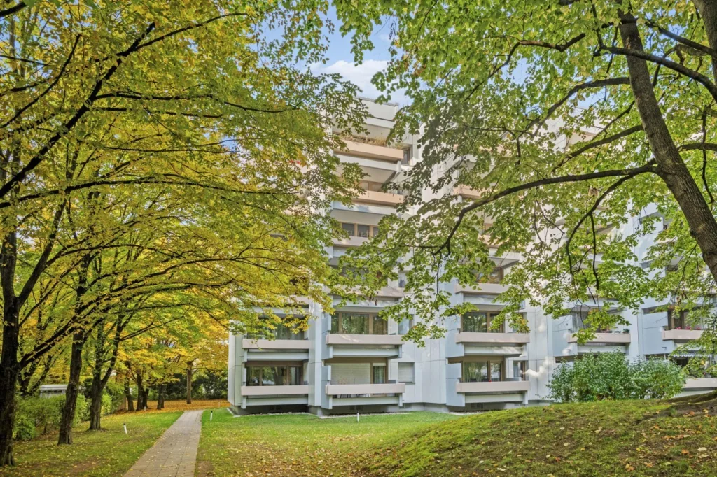Moderne Wohnanlage in München, umgeben von herbstlichen Bäumen und einem grünen Park, ideal für Kapitalanleger